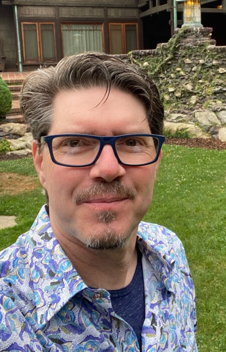 a selfie of Derek Vaughan wearing blue sleeves shirt in front of a house
